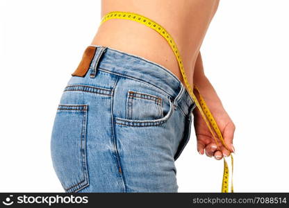 Healthy lifestyle concept - woman in blue jeans measures her perfect waistline with a measuring tape in close-up