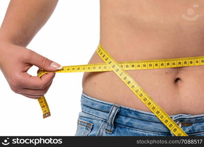 Healthy lifestyle concept - woman in blue jeans measures her waistline with a measuring tape in close-up