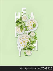 Healthy lifestyle concept. Word Healthy with water bowls with daisies flowers and green leaves at light green mint background.