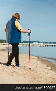 Healthy lifestyle in old age. Senior woman practicing nordic walking on sandy beach, Active elderly female enjoying warm sunny day.. Senior woman practicing nordic walking on beach