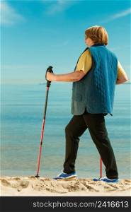 Healthy lifestyle in old age. Senior woman practicing nordic walking on sandy beach, Active elderly female enjoying warm sunny day.. Senior woman practicing nordic walking on beach
