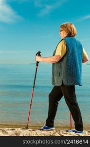 Healthy lifestyle in old age. Senior woman practicing nordic walking on sandy beach, Active elderly female enjoying warm sunny day.. Senior woman practicing nordic walking on beach