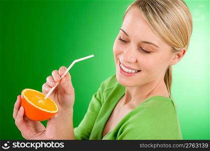 Healthy lifestyle - woman drink juice from orange with drinking straw on green background