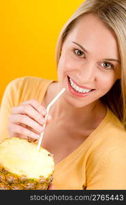 Healthy lifestyle - woman drink juice from pineapple with straw on yellow background