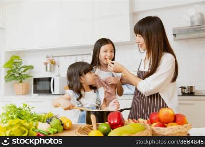 Healthy little girl child eating fruit and playing cooking with mom at home kitchen room
