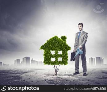 Healthy living. Image of businessman watering green house. Ecology concept