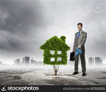 Healthy living. Image of businessman watering green house. Ecology concept