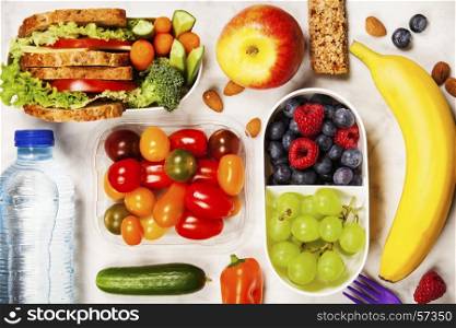 Healthy lunch box with sandwich and fresh vegetables, bottle of water and fruits on wooden background. Top view