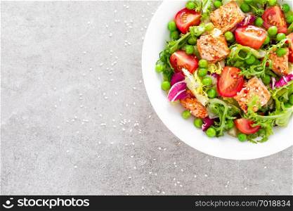 Healthy lunch vegetable salad with baked salmon fish, fresh green peas, lettuce and tomato. Top view