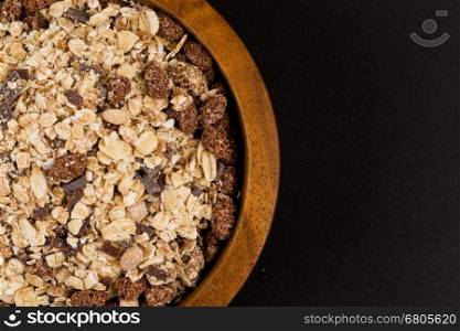 Healthy oat granola muesli cereals with chocolate in a bowl on black stone