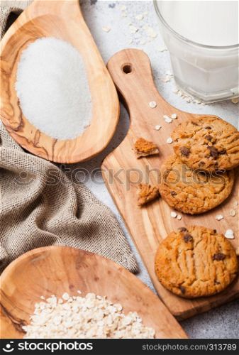 Healthy organic oat cookies with chocolate on wooden board on stone kitchen background. Sugar and raw oats in olive wooden bowl