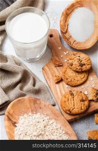 Healthy organic oat cookies with chocolate on wooden board on stone kitchen background. Sugar and raw oats in olive wooden bowl