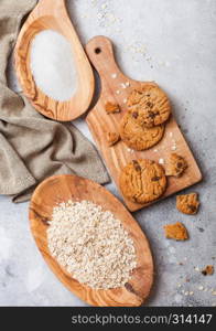 Healthy organic oat cookies with chocolate on wooden board on stone kitchen background. Sugar and raw oats in olive wooden bowl