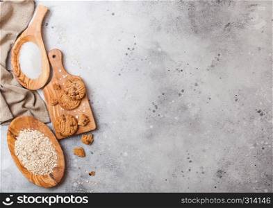 Healthy organic oat cookies with chocolate on wooden board on stone kitchen table background. Sugar and raw oats in olive wooden bowl