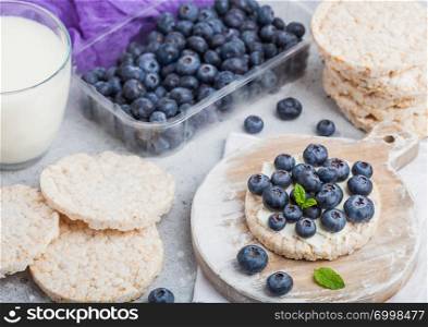 Healthy organic rice cakes with ricotta and fresh blueberries and glass of milk on light stone kitchen background.