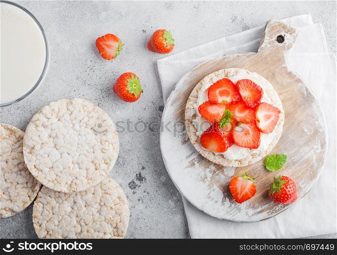 Healthy organic rice cakes with ricotta and fresh strawberries and glass of milk on light stone kitchen background.