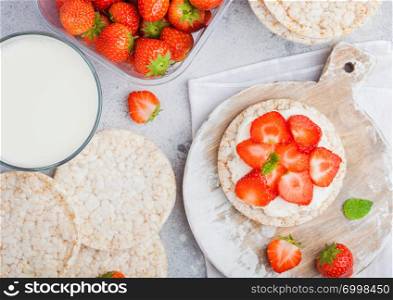 Healthy organic rice cakes with ricotta and fresh strawberries and glass of milk on light stone kitchen background.