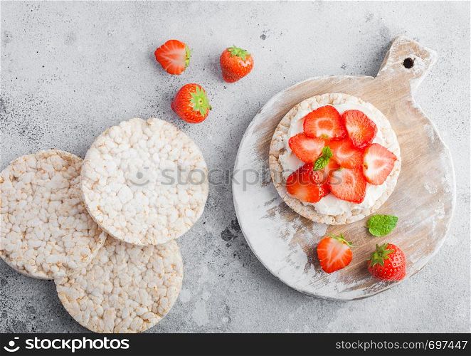 Healthy organic rice cakes with ricotta and fresh strawberries on light stone kitchen background.