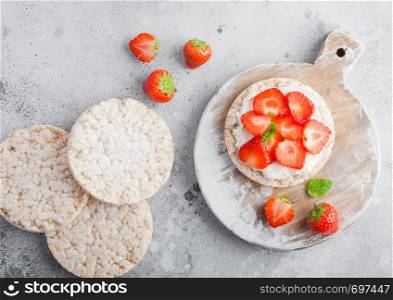 Healthy organic rice cakes with ricotta and fresh strawberries on light stone kitchen background.