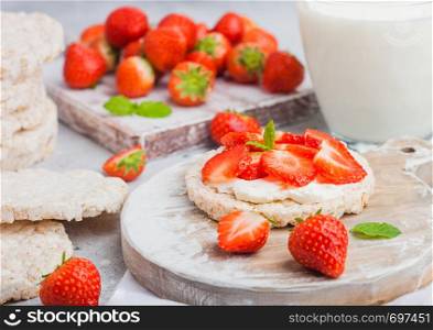 Healthy organic rice cakes with ricotta and fresh strawberries on wooden board and glass of milk on light stone kitchen background.
