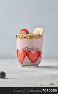 Healthy pink smoothie in glasses with natural fruits: strawberry, banana, blueberry, oat flakes and chia seeds on grey background. Superfoods, natural detox, diet and healthy food.. Organic yogurt smoothie with strawberries, banana, blueberry, oat flakes and chia seeds, fruit dessert on grey background