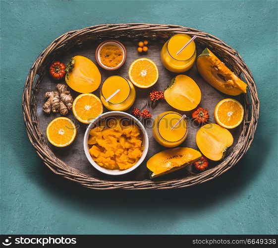 Healthy pumpkin smoothie in glasses with orange color ingredients : persimmon , orange fruits, ginger and turmeric powder in wooden tray, top view. Immune boosting detox beverage for cold season