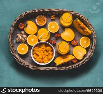 Healthy pumpkin smoothie in glasses with orange color ingredients : persimmon , orange fruits, ginger and turmeric powder in wooden tray, top view. Immune boosting detox beverage for cold season