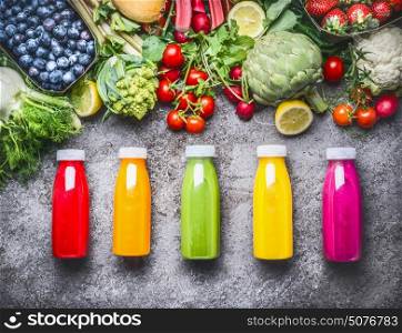 Healthy red, orange, green, yellow and pink Smoothies and juices in Bottles on grey concrete background with fresh organic vegetables , fruits and berries ingredients, top view