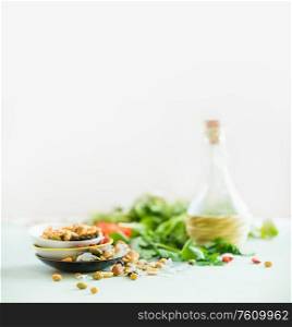 Healthy salad making ingredients on white table at light sunny wall background. Fresh kitchen herbs. Nuts topping. Olives oil. Salad dressing . Diet or vegetarian food concept.