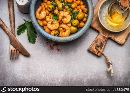 Healthy salad with Chickpeas, olives and shrimps in bowl and cutlery on gray concrete background, top view, border