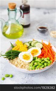 Healthy salad with couscous, carrots, cucumber, green beans, soybeans, corn and an egg on a gray concrete background. Food and health. Buddha bowl salad. Organic natural foods. Plant-based dishes.