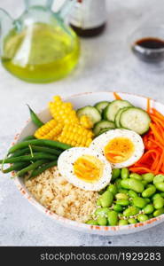 Healthy salad with couscous, carrots, cucumber, green beans, soybeans, corn and an egg on a gray concrete background. Food and health. Buddha bowl salad. Organic natural foods. Plant-based dishes.