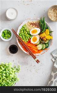 Healthy salad with couscous, carrots, cucumber, green beans, soybeans, corn and an egg on a gray concrete background. Food and health. Buddha bowl salad. Organic natural foods. Plant-based dishes.