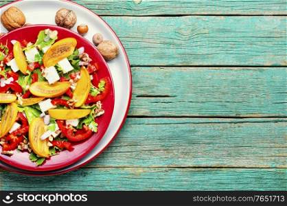 Healthy salad with persimmon and feta cheese.Seasonal salad on wooden table.Space for text. Fresh persimmon salad
