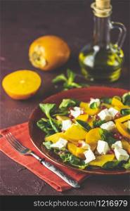 Healthy salad with persimmon, doucette (lambs-lettuce, cornsalad, feld salad) and feta cheese on a red plate on a red background. Superfoods Vitamin autumn or winter persimmon salad.