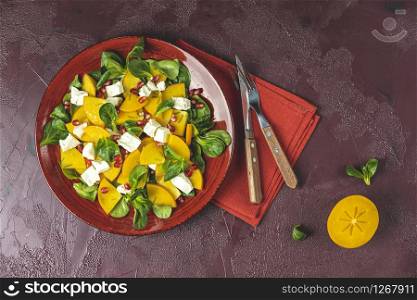 Healthy salad with persimmon, doucette (lambs-lettuce, cornsalad, feld salad) and feta cheese. Fitness food, superfoods vitamin persimmon salad. Top view, flat lay, copy space.