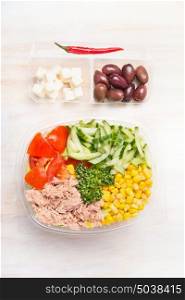 Healthy salad with tuna and vegetables in plastic packaging for diet lunch on white wooden background, top view