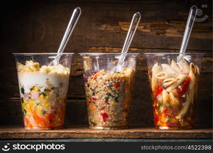 Healthy salads in plastic cups with fork on dark rustic background, side view. Take away lunch