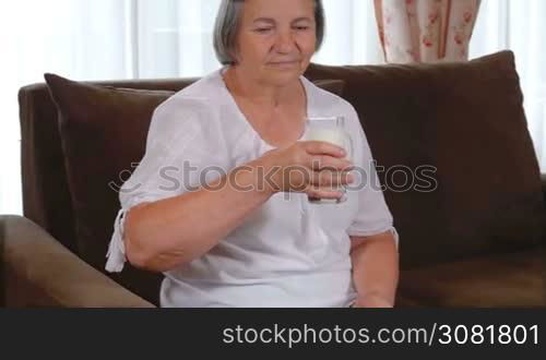 Healthy senior lady drinking a glass of fresh milk with a smile of appreciation and enjoyment as she looks at the camera. Healthy bones concept. Slow motion