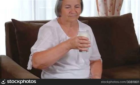 Healthy senior lady drinking a glass of fresh milk with a smile of appreciation and enjoyment as she looks at the camera. Healthy bones concept. Slow motion