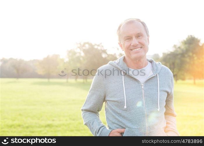 Healthy senior man in hooded jacket smiling at park