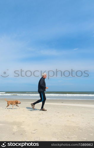 Healthy senior man running with his dog at the beach in winter