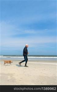 Healthy senior man running with his dog at the beach in winter