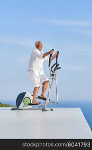 healthy senior man working out on gym treadmill machine at modern home terace with ocean view