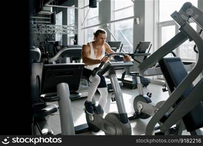 Healthy smiling sportsman using elliptical machine at gym fitness center. Happy motivated male bodybuilder doing aerobic exercise for slim and firm healthy body. Healthy smiling sportsman using elliptical machine at gym fitness center
