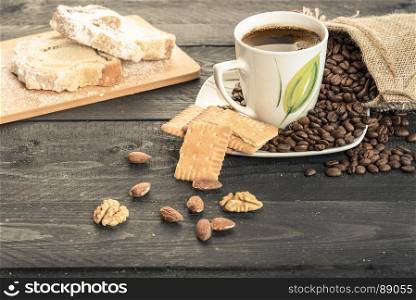 Healthy snack with slices of pound cake, biscuits, almonds, walnuts and a cup of coffee on a plate covered with coffee beans