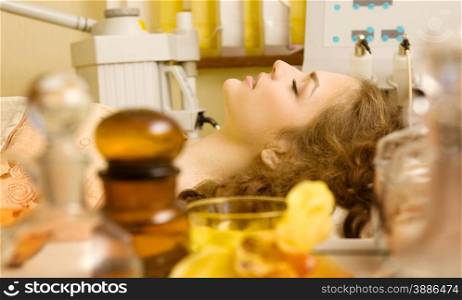 Healthy spa: composition with different oil bottles and yellow orchid on the foreground and beautiful woman having beauty treatment on the background.
