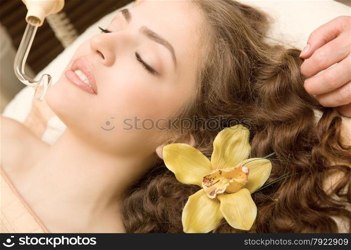 Healthy spa; young relaxing beautiful woman having facial treatment, with orchid in the long brown hair