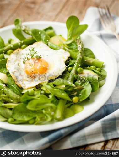 Healthy spring green salad with egg served on white plate