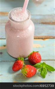 Healthy strawberry smoothie in a mason glass jar with scattered fruits over a rustic wood background